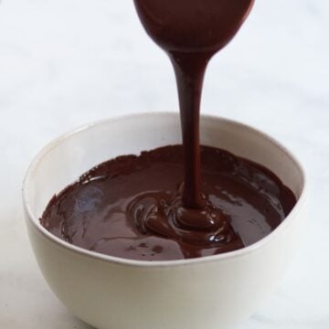 shimmery liquid chocolate ganache is poured from a ladle into a white bowl.