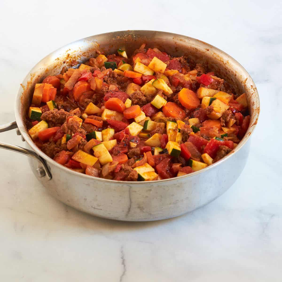 chopped vegetables with zucchini and ground beef in skillet.