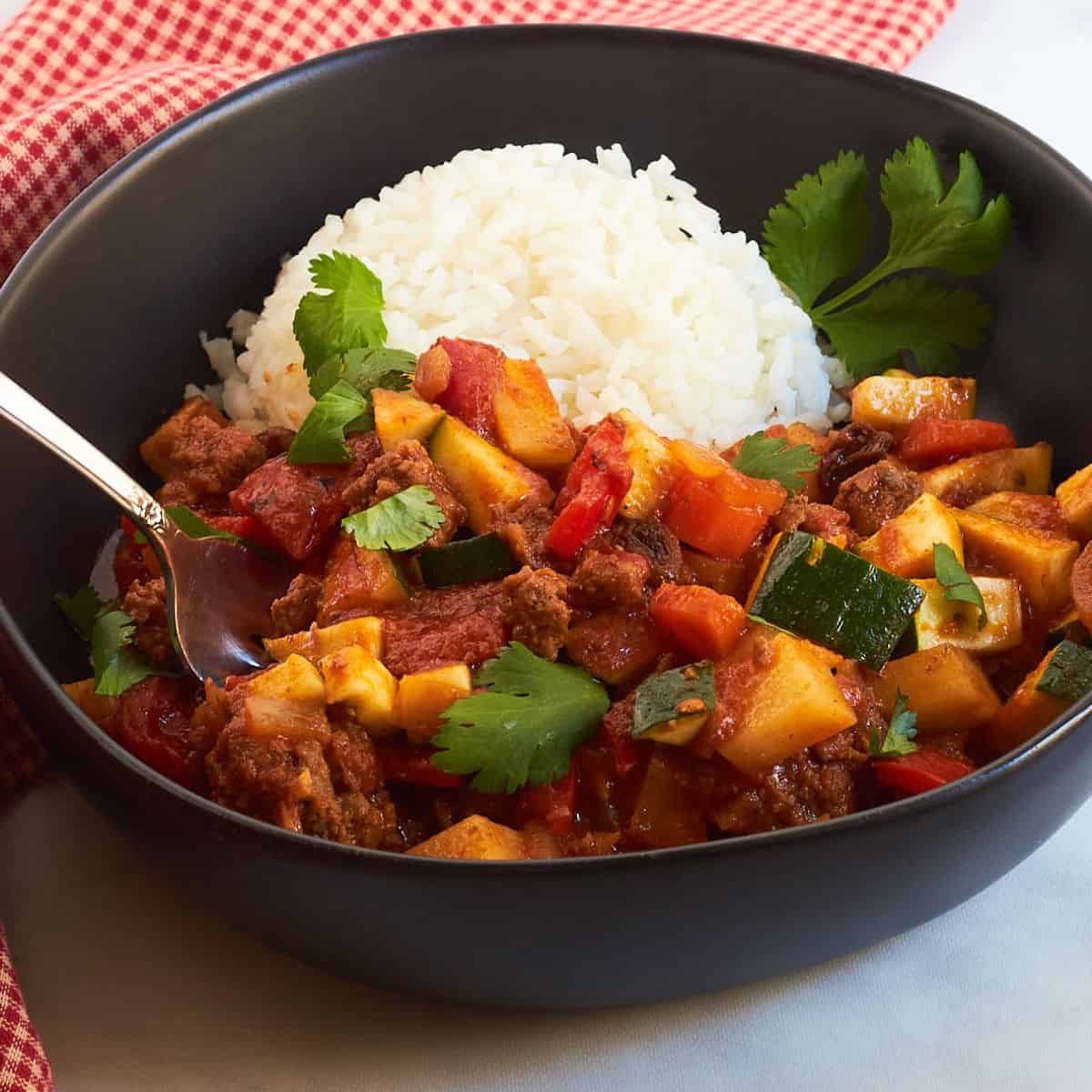 Cuban Picadillo with potatoes, raisins, and olives, in a black bowl with rice.