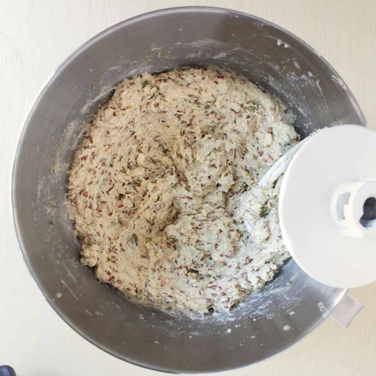 dough hook from a stand mixer in a bowl of very moist, seeded batter.