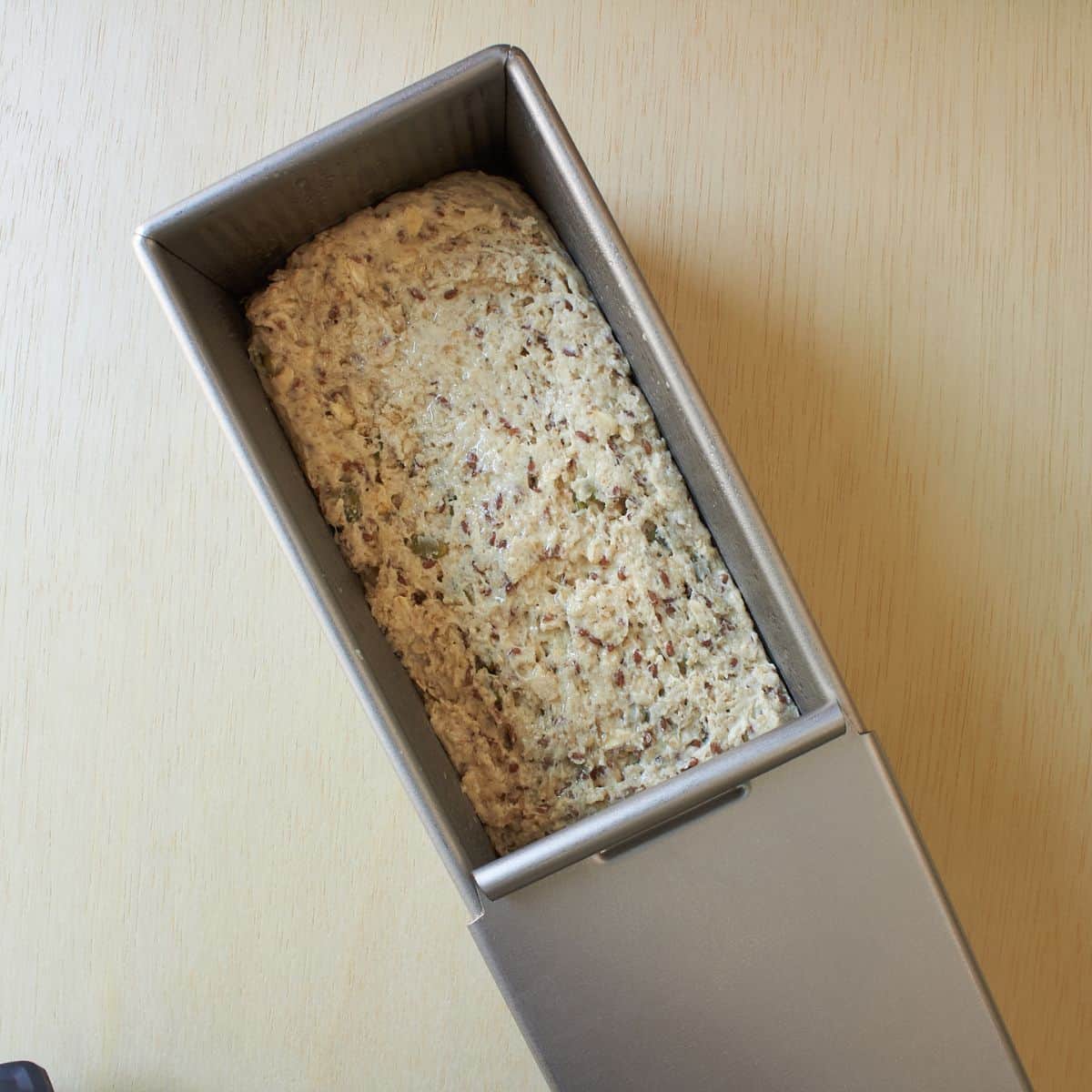 moist, seeded bread dough in metal loaf pan.