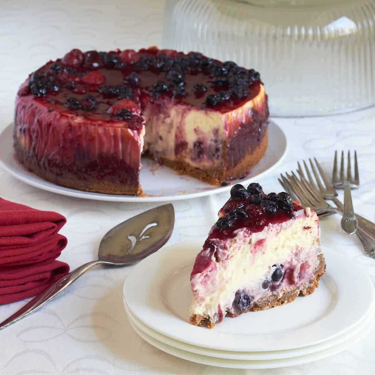 mixed berry cheesecake with a single slice served, on white plates.