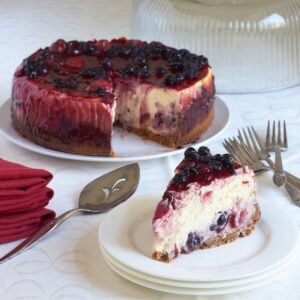 mixed berry cheesecake with a single slice served, on white plates.