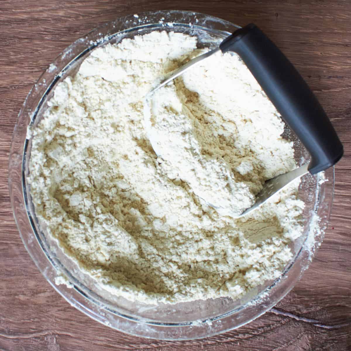pastry blender resting in glass bowl of dry flour mixture.