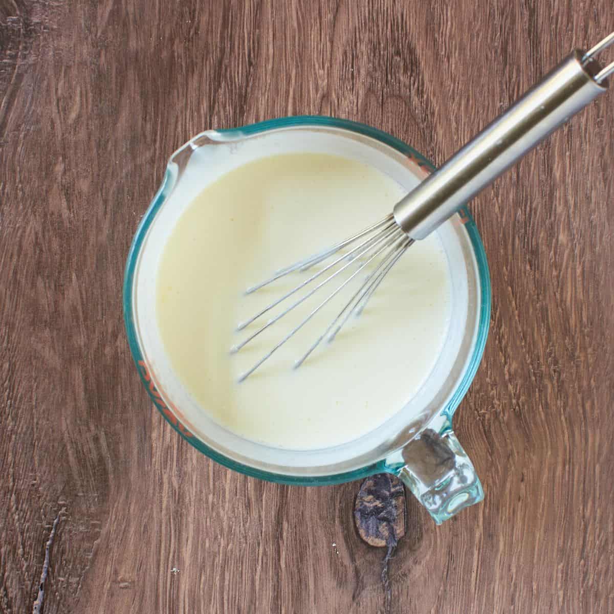 whisk resting in measuring cup of milk.