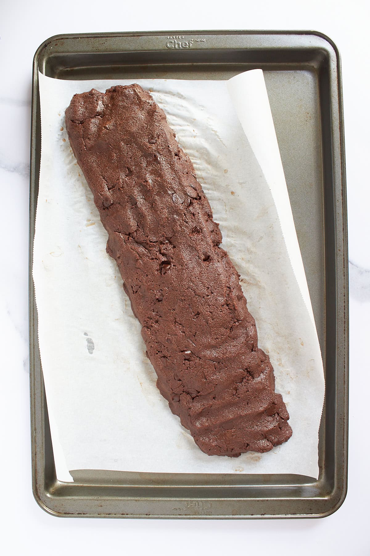 long, flattish shaped chocolate dough on parchment-lined baking sheet.