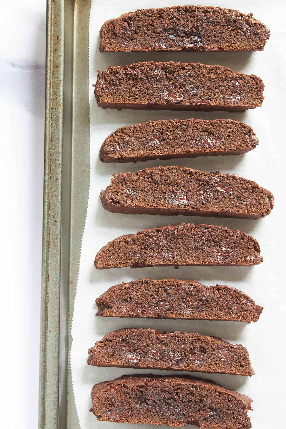 sliced gluten-free chocolate biscotti on parchment-lined baking sheet.