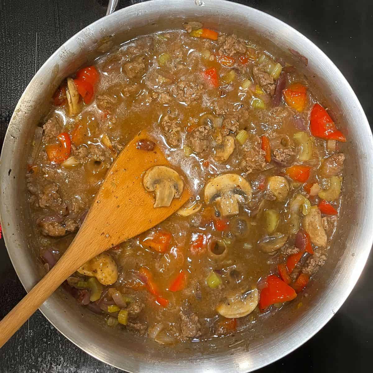 chopped vegetables and ground beef in sauce in pan.