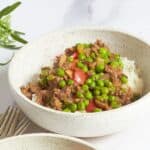 mixture of ground beef, red pepper, and green peas on rice in white bowl.