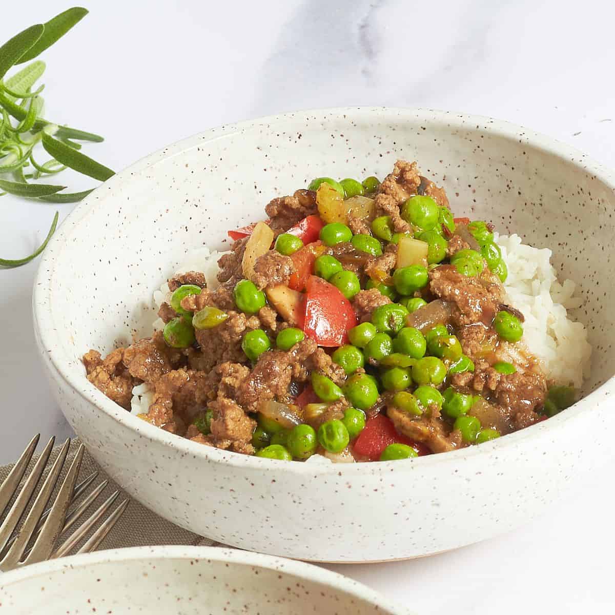 mixture of ground beef, red pepper, and green peas on rice in white bowl.