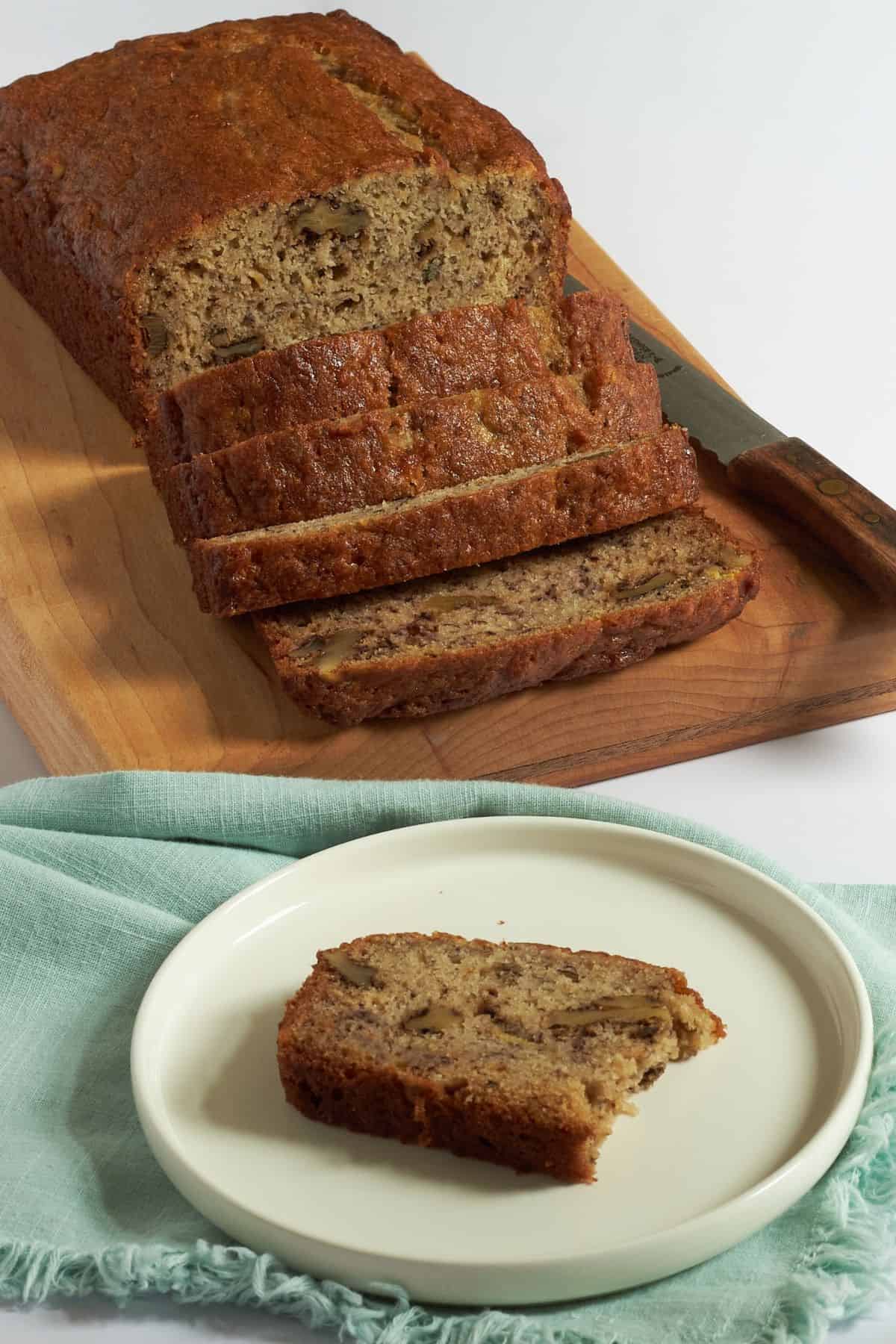 partially sliced gluten-free banana bread with a piece on a white plate.